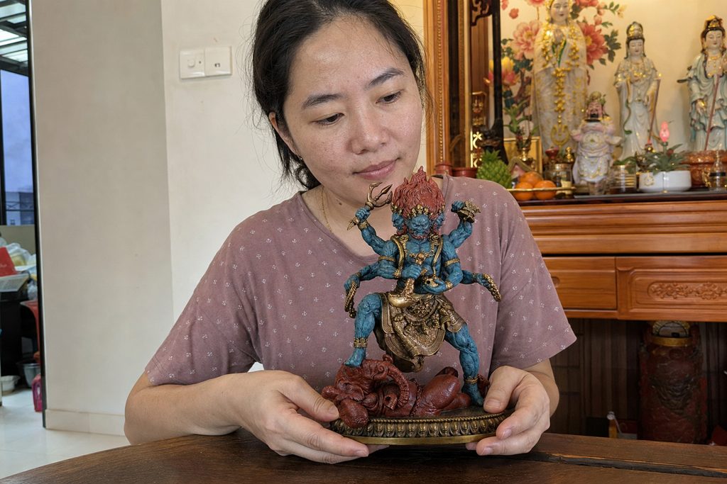 Six-armed Mahakala statue supported by a Chinese woman in a home altar setting